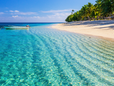 Pristine white-sand beach with transparent lagoon waters and a small boat anchored near the shoreline