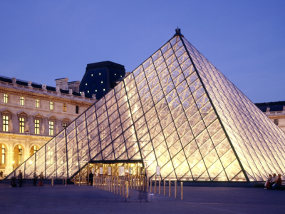 The iconic glass pyramid entrance of the Louvre Museum beautifully illuminated at dusk, surrounded by the historic Louvre Palace in Paris.