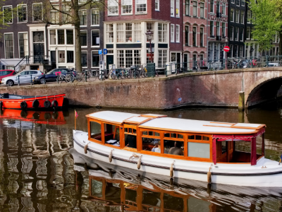 Traditional sightseeing boat cruising along Amsterdam's historic canal beside brick bridges and classic Dutch houses